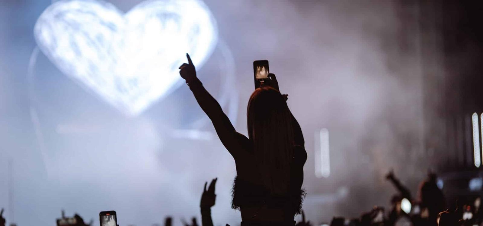 Ferrara Summer Festival: una ragazza alza il telefono verso il palco, dietro un cuore di luce